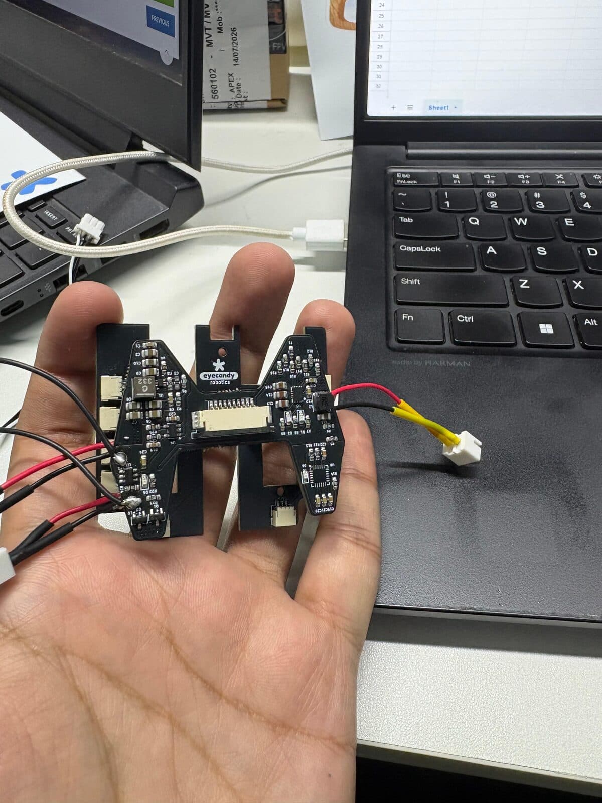 A small multi-board electronics assembly held in one hand, its four boards arranged around a central spine and wired to power and ribbon connectors.